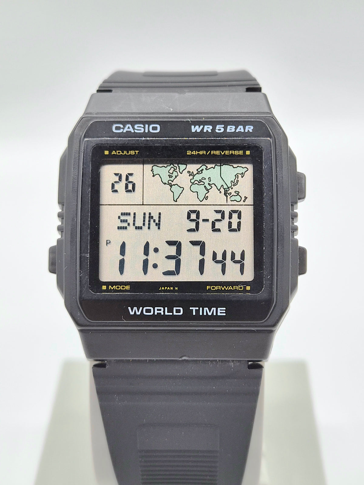 A Casio World Time digital watch with a dark gray resin case and strap, featuring a light-colored display screen showing the time and date.