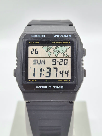 A Casio World Time digital watch with a dark gray resin case and strap, featuring a light-colored display screen showing the time and date.