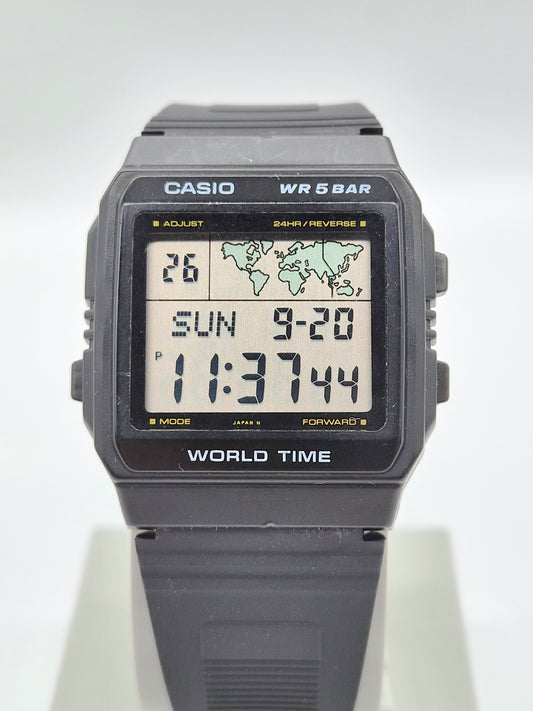 A Casio World Time digital watch with a dark gray resin case and strap, featuring a light-colored display screen showing the time and date.