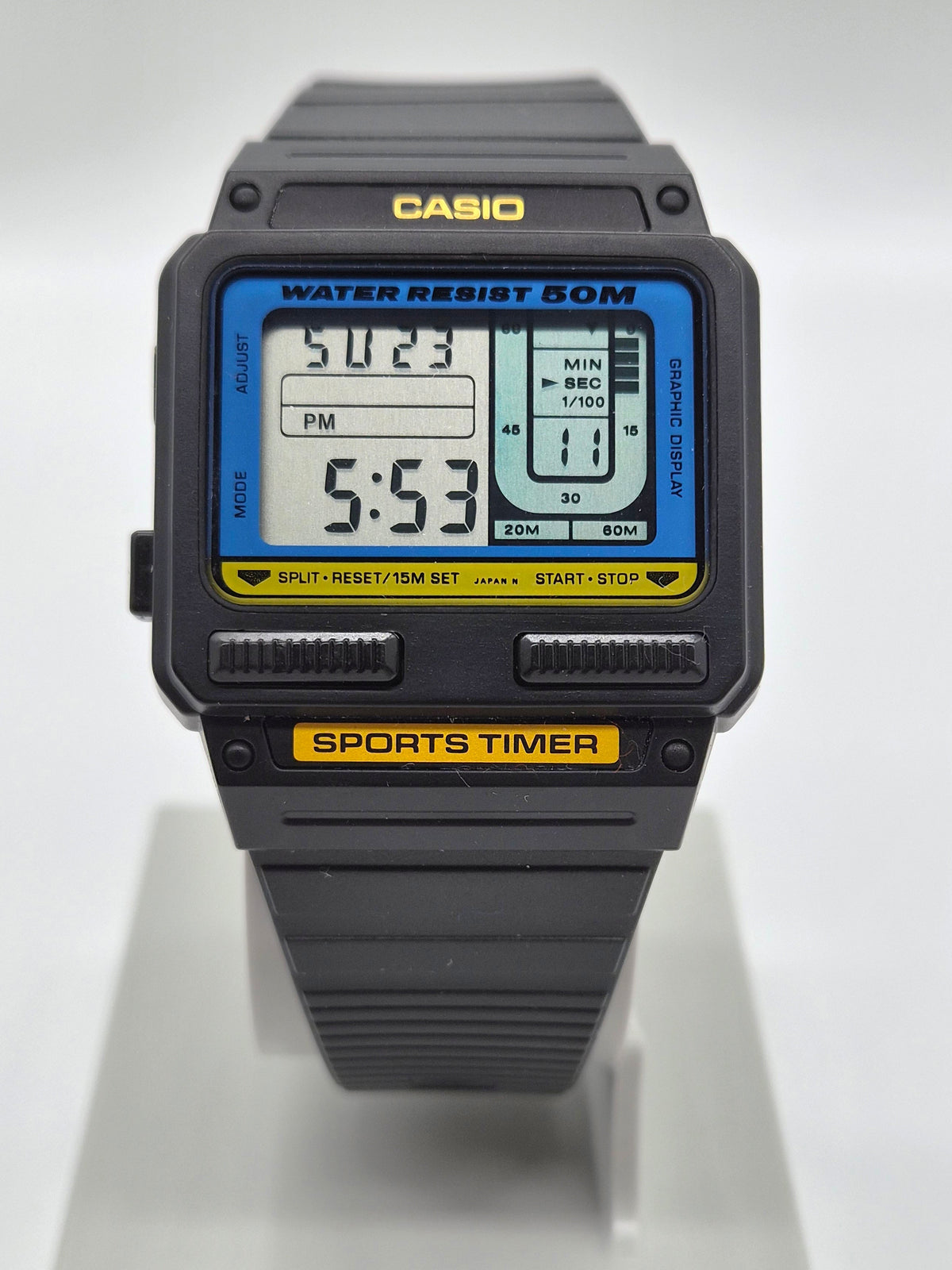 A Casio sports watch with a black plastic case and strap, featuring a blue and yellow digital display screen, shown on a white display stand.