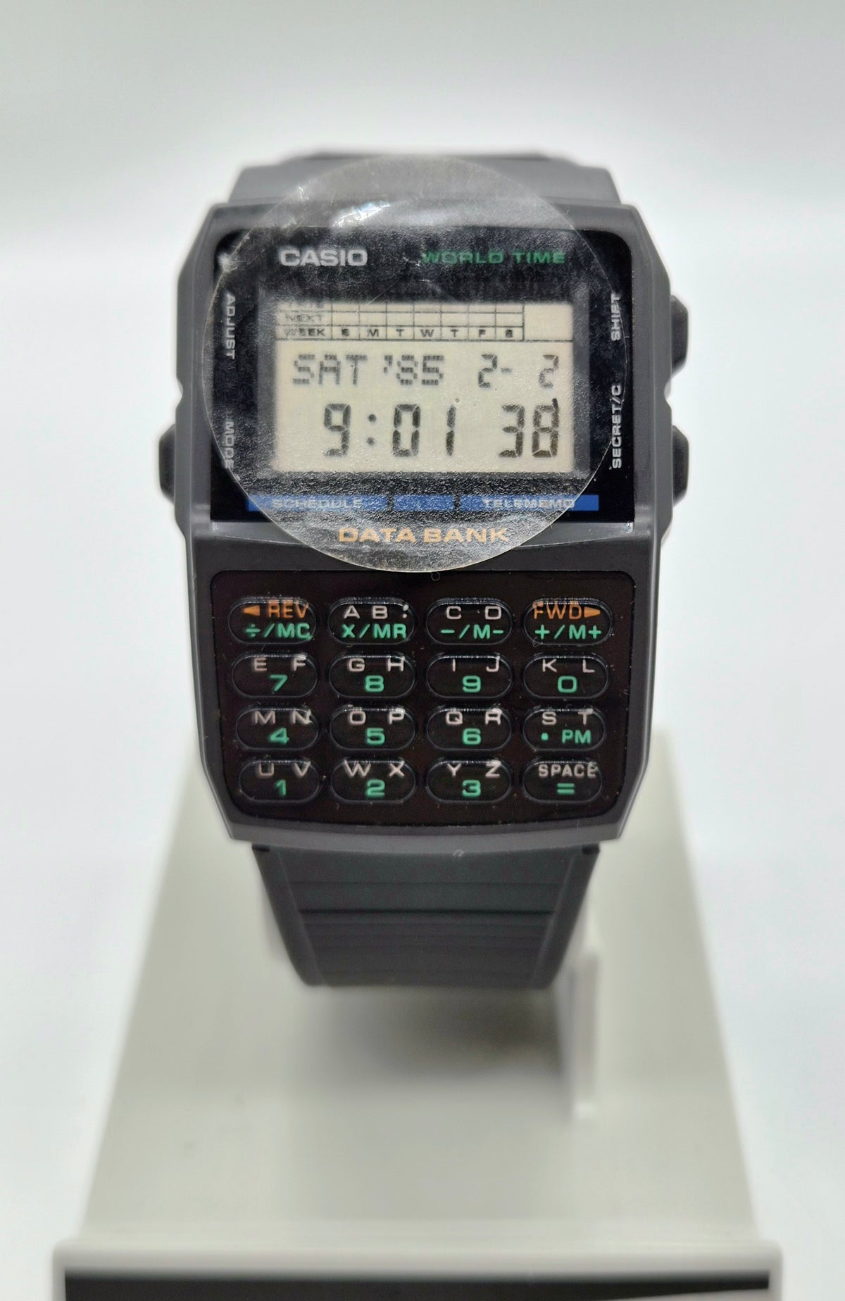 A Casio World Time digital watch with a black plastic body, numeric keypad, and LCD display, shown standing on a light gray display stand against a white background.