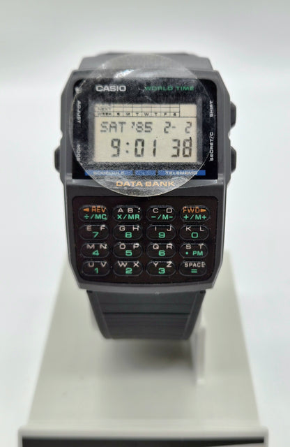 A Casio World Time digital watch with a black plastic body, numeric keypad, and LCD display, shown standing on a light gray display stand against a white background.