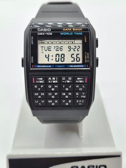 A Casio DX-108 World Time digital watch with a black strap and case, featuring a built-in numeric keypad on the front face, displayed on a white stand.