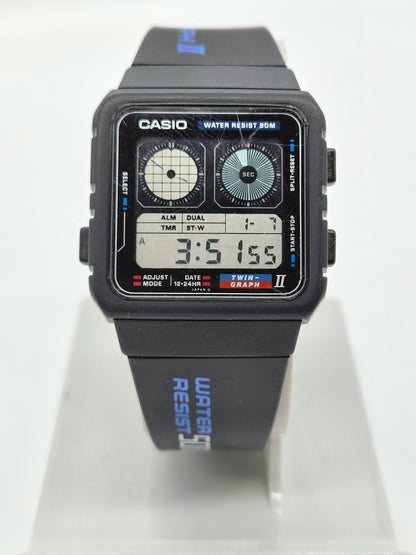 A Casio digital wrist watch with a black rectangular case and strap, featuring a dual analog-digital face and blue printed text on the strap, displayed on a clear stand against a white background.