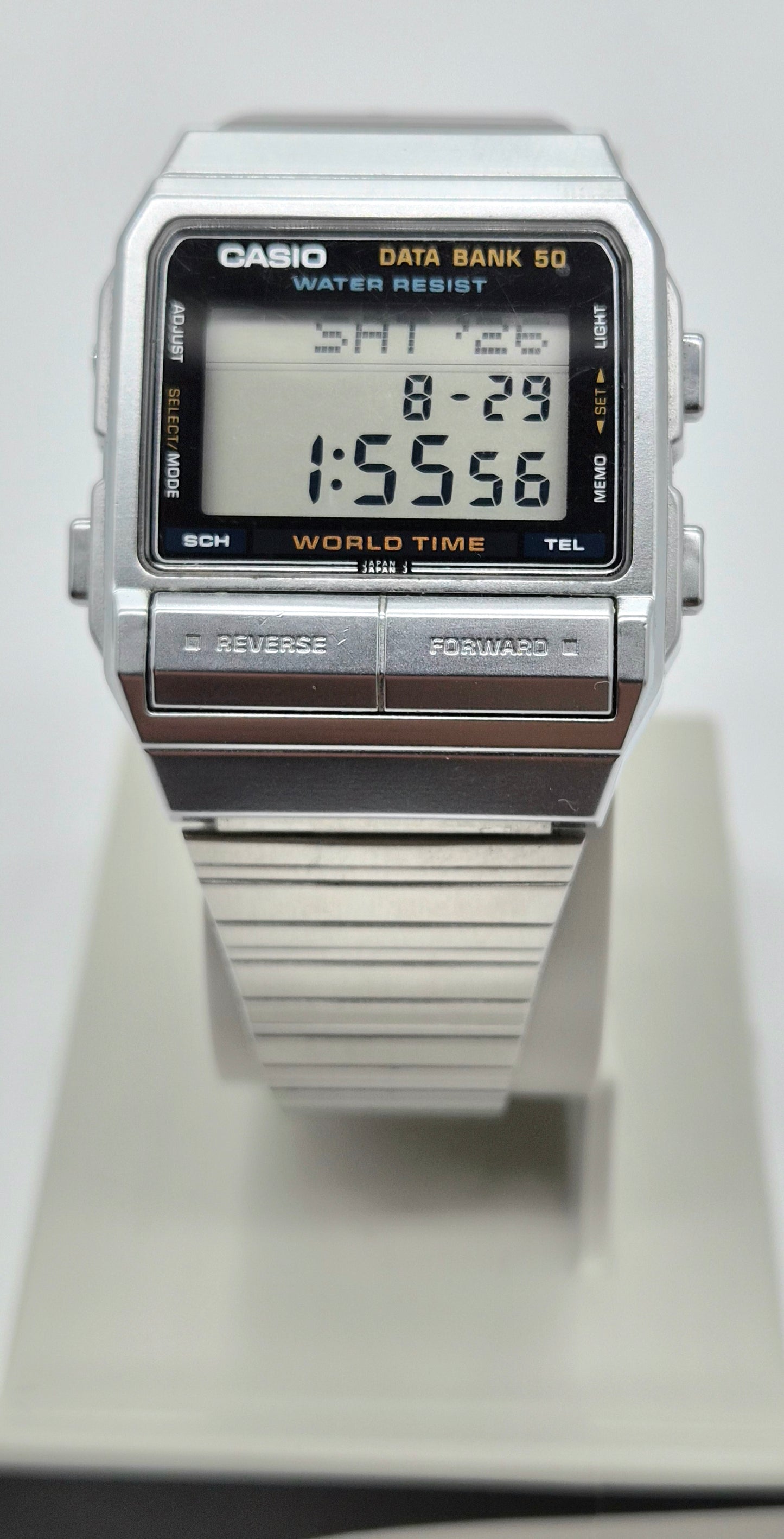 A Casio digital Databank DB 520 watch with a silver-tone metal case and strap, featuring a black face with orange text and a digital display showing the time 1:55:56.