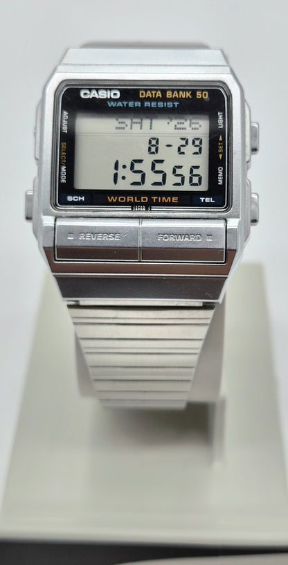 A Casio digital Databank DB 520 watch with a silver-tone metal case and strap, featuring a black face with orange text and a digital display showing the time 1:55:56.