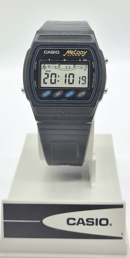 A black Casio Metody digital-analog watch with a black strap, displayed on a white stand with a branded base against a white background.