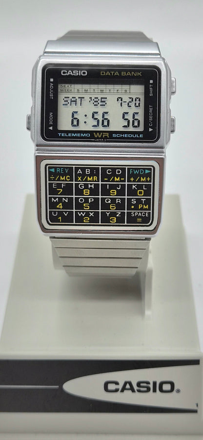A vintage Casio Data Bank calculator watch with a silver-tone metal case, black face, and a built-in calculator keypad on the lower half, displayed on a white Casio stand against a light gray background.