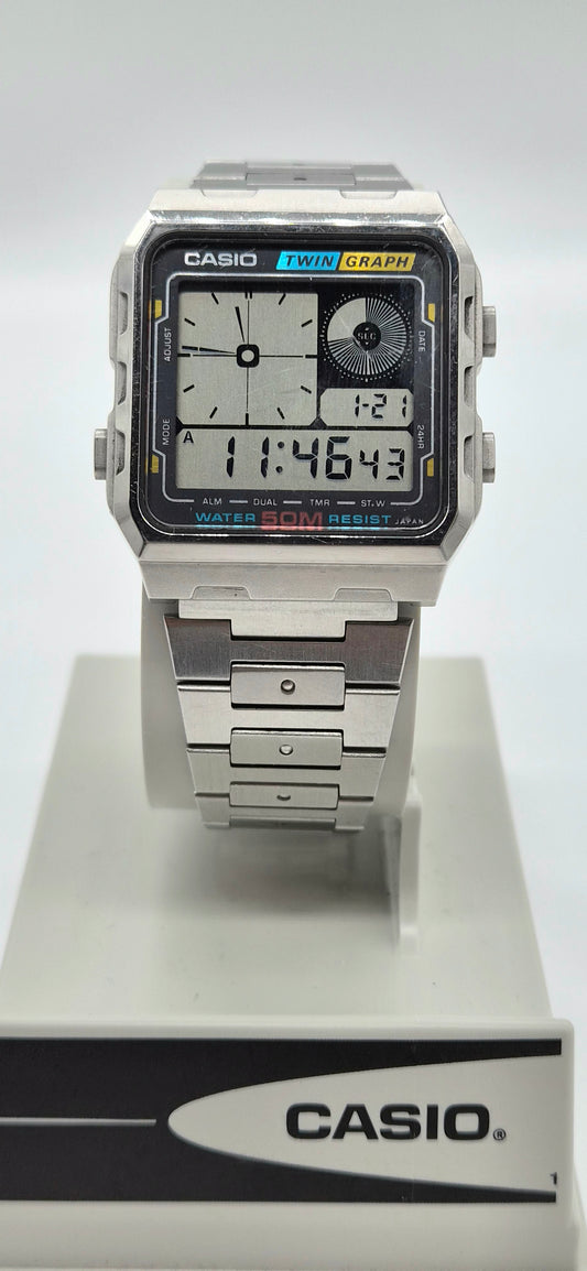 A Casio dual display analog watch with a silver-toned metal case and link bracelet, mounted on a white display stand with a Casio-branded base.