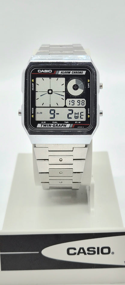 A Casio dual display analog-digital wristwatch with a silver-tone metal case and bracelet, shown standing on a white display stand with a branded base.