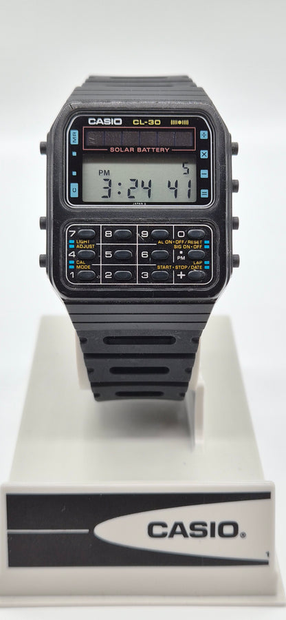 A Casio CL-30 solar battery digital watch with a black strap and case, featuring a gray LCD display and yellow accents, shown on a white display stand with a Casio logo.