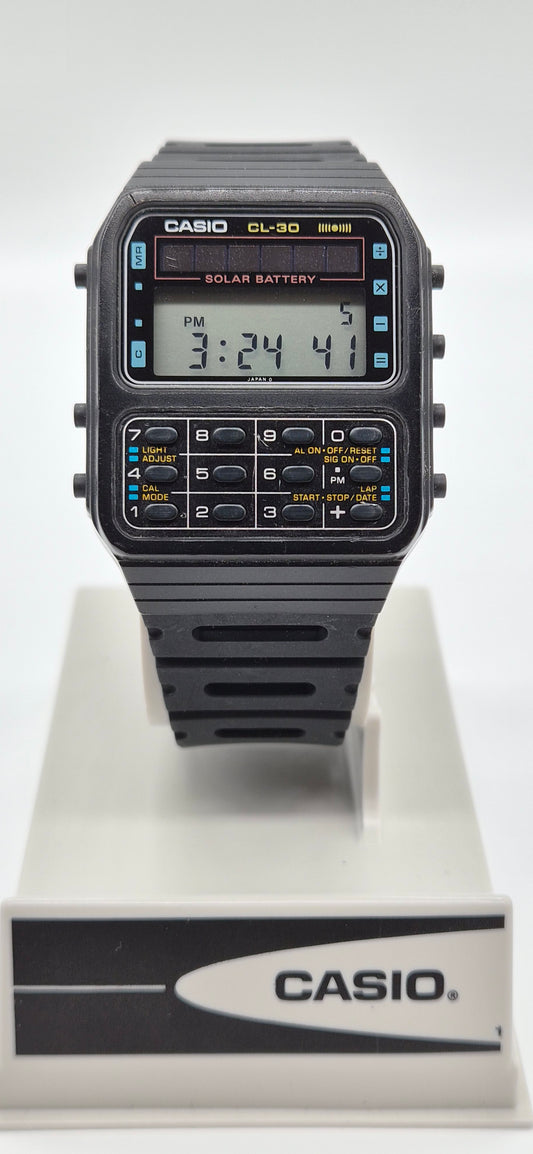 A Casio CL-30 solar battery digital watch with a black strap and case, featuring a gray LCD display and yellow accents, shown on a white display stand with a Casio logo.
