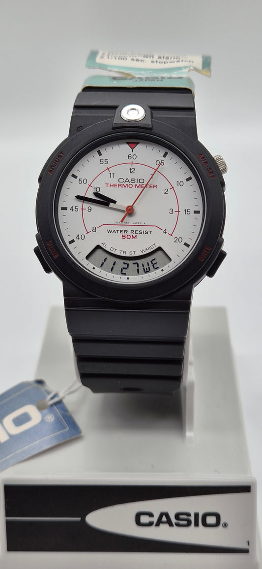 A Casio analog watch with a black resin case and strap, featuring a white dial with red accents and a digital day window, displayed on a white stand with a Casio-branded box.
