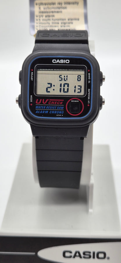 A Casio digital wrist watch with a black strap and case, featuring blue bezel detailing, a red circular button, and a digital display showing the time 2:10:13.