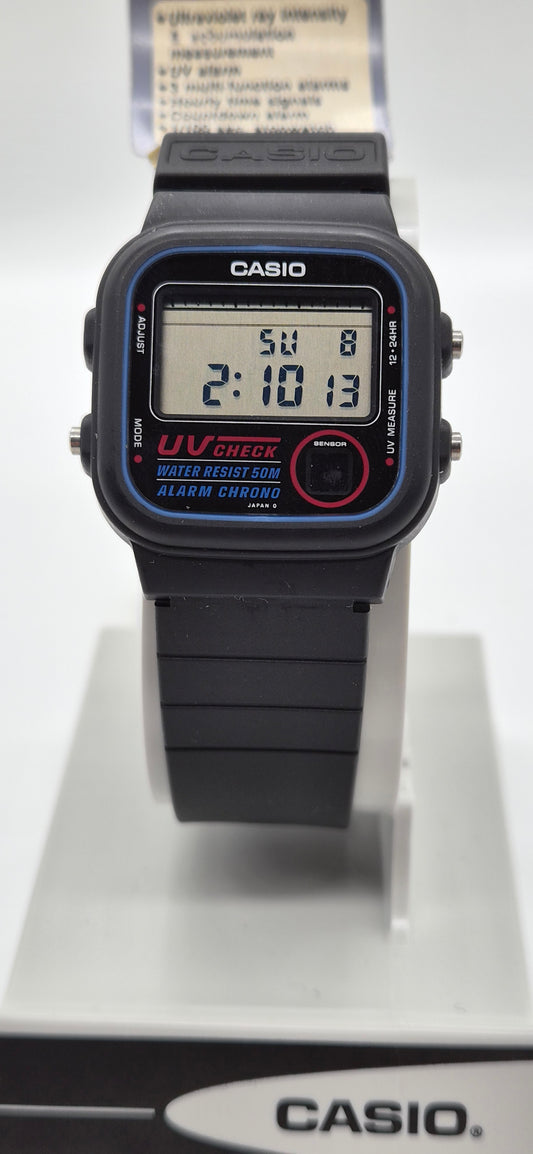 A Casio digital wrist watch with a black strap and case, featuring blue bezel detailing, a red circular button, and a digital display showing the time 2:10:13.